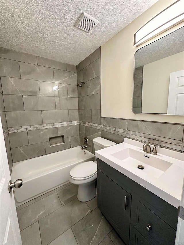 full bathroom with a textured ceiling, toilet, vanity, tile walls, and tiled shower / bath