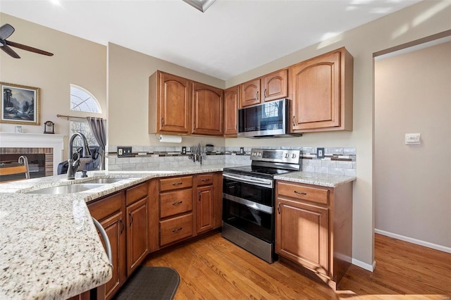 kitchen with appliances with stainless steel finishes, light stone counters, ceiling fan, sink, and light hardwood / wood-style floors