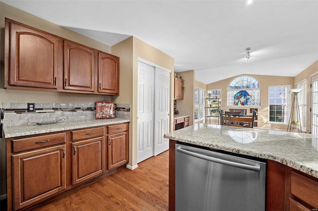 kitchen featuring decorative backsplash, light stone counters, vaulted ceiling, light hardwood / wood-style flooring, and dishwasher