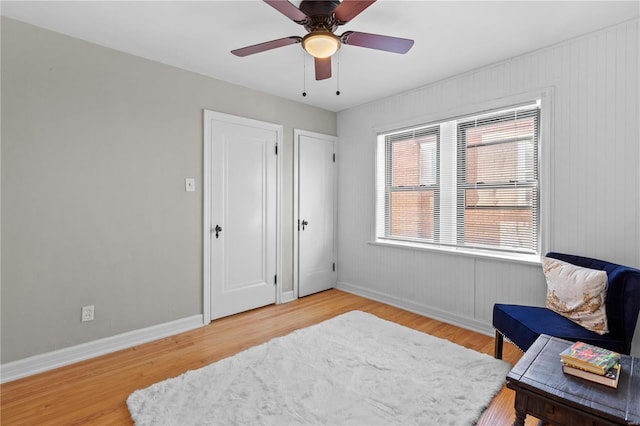 living area with ceiling fan, hardwood / wood-style floors, and wood walls