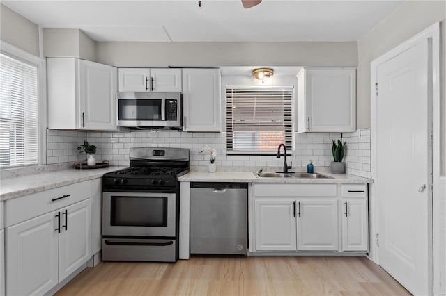 kitchen with sink, stainless steel appliances, light hardwood / wood-style flooring, backsplash, and white cabinets