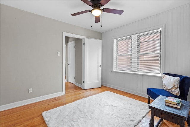 sitting room with ceiling fan, light hardwood / wood-style flooring, and wood walls