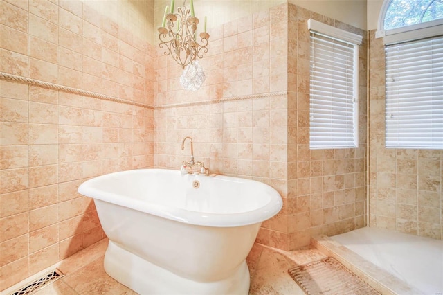 bathroom with a bathing tub, a wealth of natural light, a notable chandelier, and tile walls