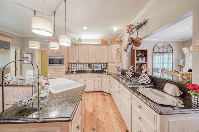 kitchen featuring pendant lighting, stainless steel microwave, sink, dark stone countertops, and a kitchen island with sink