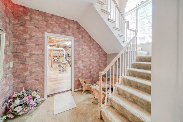 carpeted foyer with lofted ceiling and brick wall