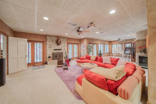 carpeted living room featuring ceiling fan, plenty of natural light, a fireplace, and a drop ceiling