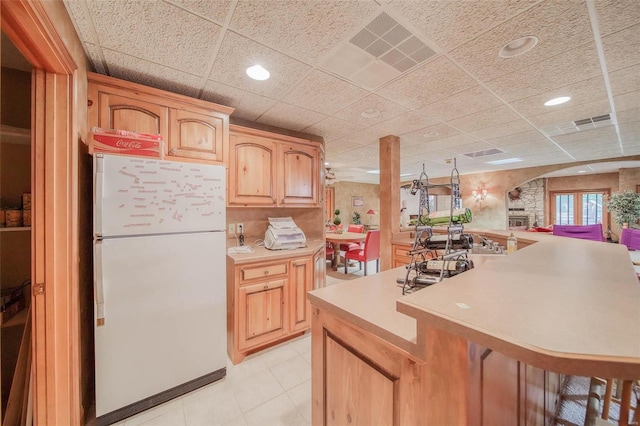 kitchen with a drop ceiling, a breakfast bar area, light brown cabinets, and white refrigerator