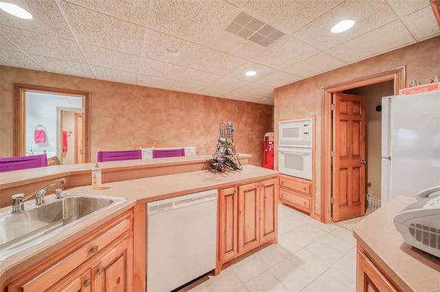 kitchen with sink, light brown cabinetry, a drop ceiling, and white appliances