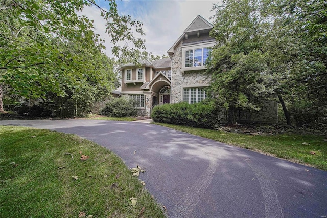 view of front facade with stone siding, a front yard, and driveway