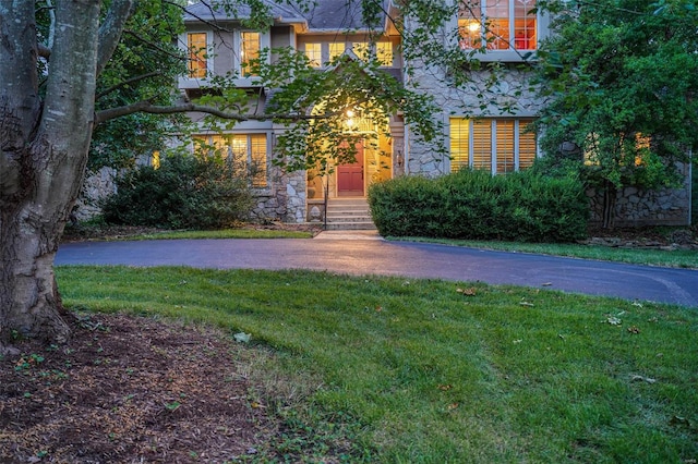 view of front of property with entry steps, stone siding, a front lawn, and driveway