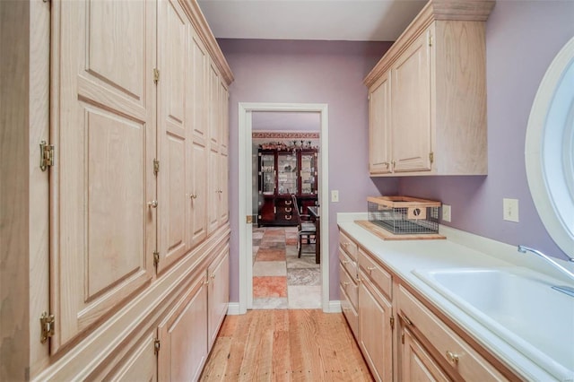 interior space featuring light brown cabinets, a sink, baseboards, light wood-style floors, and light countertops