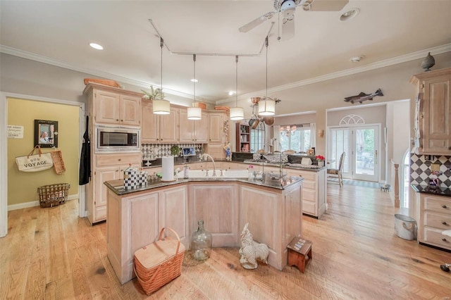 kitchen featuring backsplash, light brown cabinetry, stainless steel microwave, a center island with sink, and pendant lighting