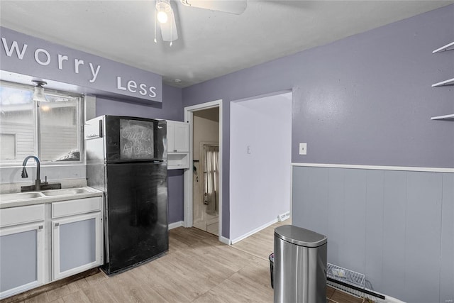 kitchen featuring white cabinets, black fridge, sink, wooden walls, and ceiling fan