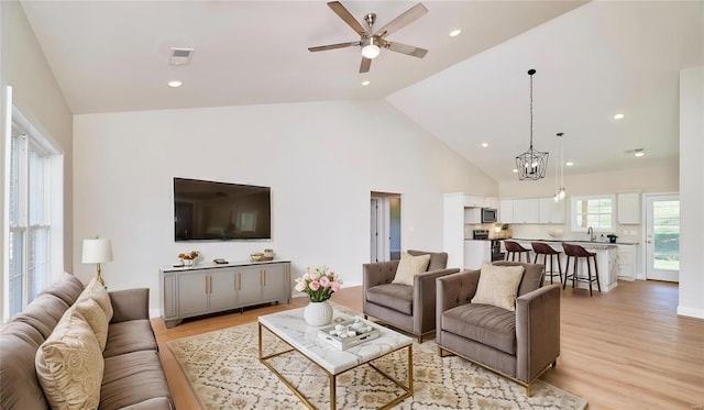 living room featuring ceiling fan with notable chandelier, light wood-type flooring, sink, and high vaulted ceiling