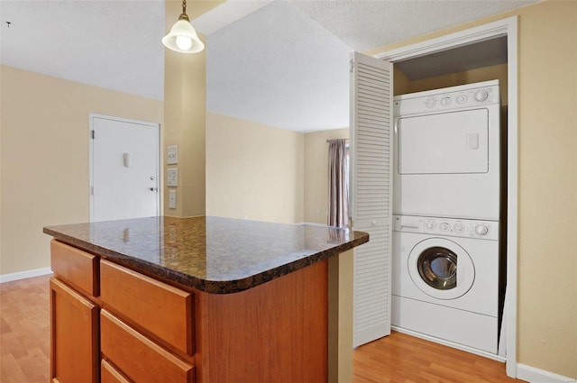 kitchen featuring a center island, light hardwood / wood-style flooring, stacked washer and dryer, pendant lighting, and a textured ceiling