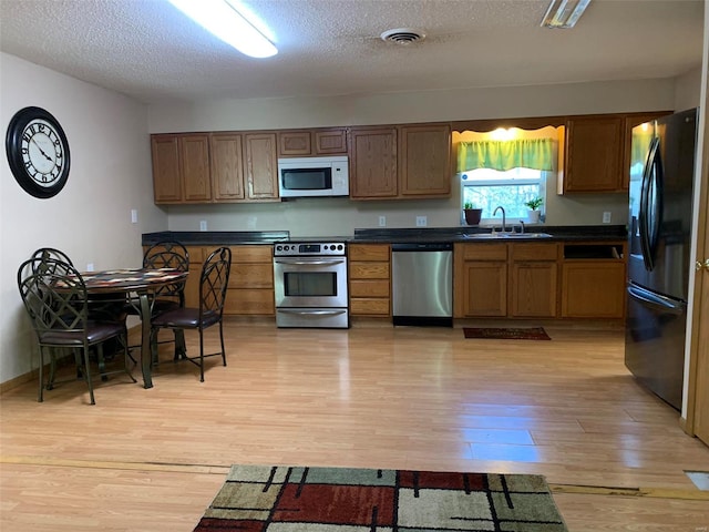 kitchen featuring sink, stainless steel appliances, a textured ceiling, and light wood-type flooring