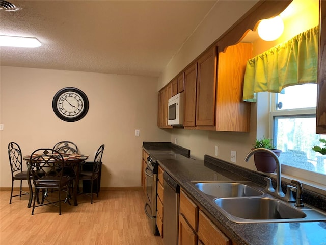 kitchen featuring appliances with stainless steel finishes, a textured ceiling, light hardwood / wood-style floors, and sink