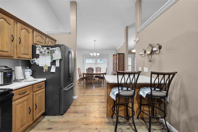 kitchen with a kitchen breakfast bar, a chandelier, decorative light fixtures, light hardwood / wood-style floors, and black appliances