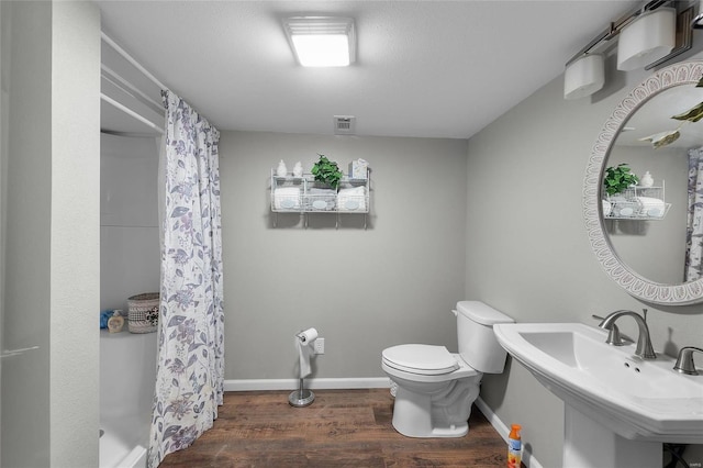 bathroom with a shower with shower curtain, wood finished floors, baseboards, a sink, and toilet