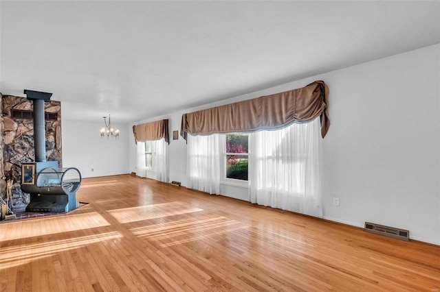 unfurnished living room with a notable chandelier, a wood stove, and hardwood / wood-style floors