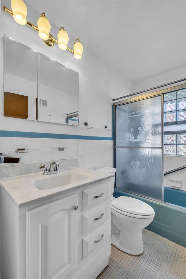 full bathroom with toilet, tile walls, tile patterned flooring, shower / bath combination with glass door, and vanity