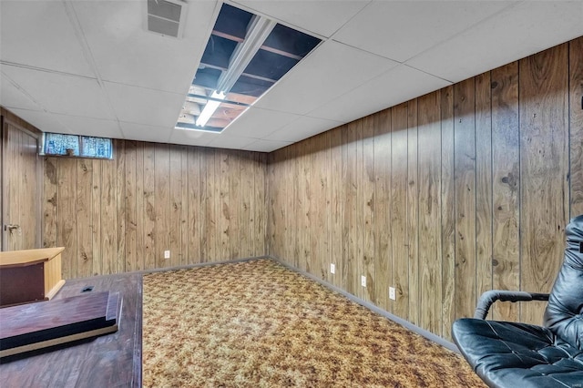 basement with carpet floors, a paneled ceiling, and wooden walls