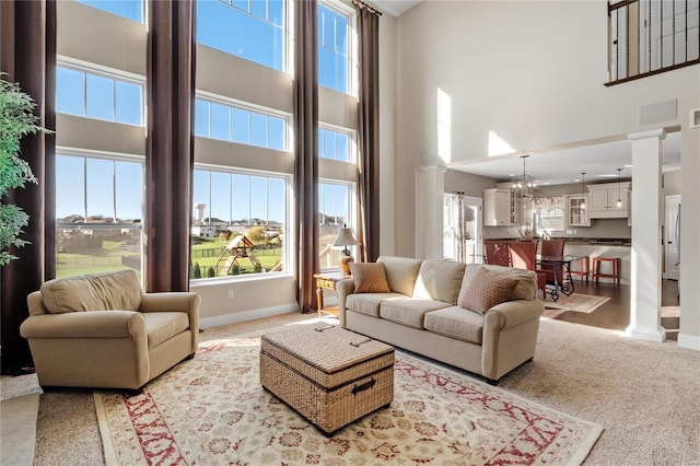 carpeted living room featuring ornate columns, a high ceiling, and an inviting chandelier