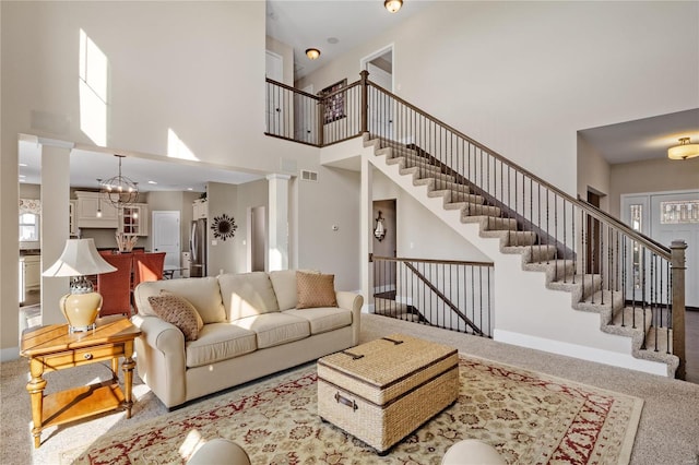 carpeted living room featuring decorative columns, a high ceiling, and a notable chandelier