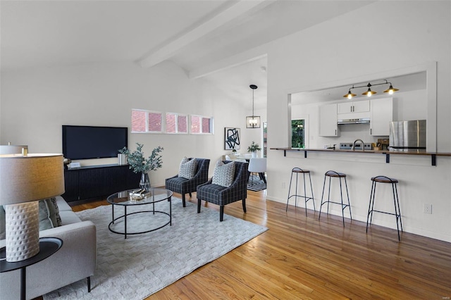 living room with lofted ceiling with beams, an inviting chandelier, and light hardwood / wood-style flooring