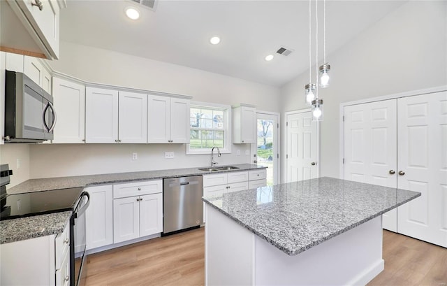 kitchen featuring lofted ceiling, white cabinets, sink, appliances with stainless steel finishes, and a kitchen island