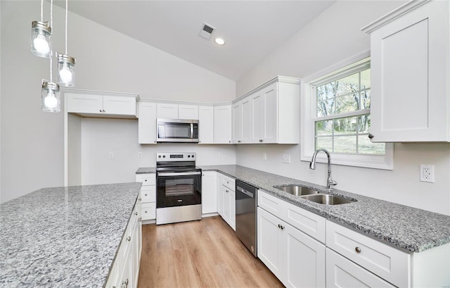 kitchen with pendant lighting, sink, vaulted ceiling, white cabinetry, and stainless steel appliances