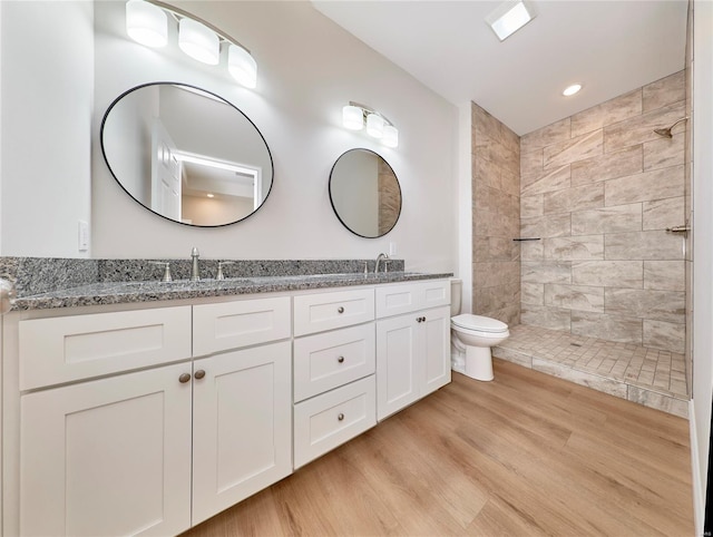 bathroom with hardwood / wood-style floors, vanity, toilet, and a tile shower