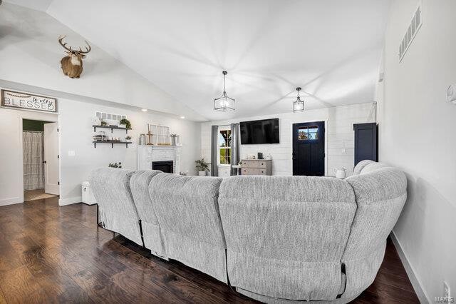 living room with dark hardwood / wood-style floors, vaulted ceiling, and a brick fireplace