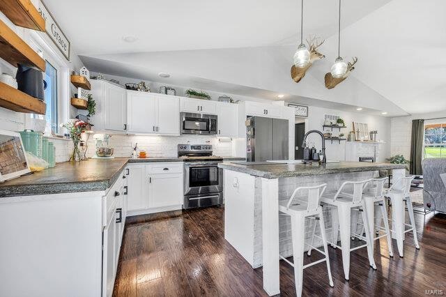 kitchen with a center island, stainless steel appliances, vaulted ceiling, and white cabinetry