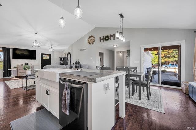 kitchen featuring a kitchen breakfast bar, stainless steel dishwasher, a center island with sink, white cabinets, and lofted ceiling