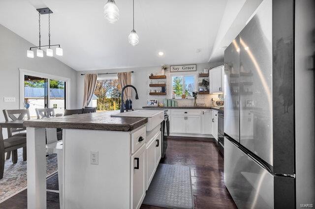 kitchen with white cabinets, stainless steel fridge, pendant lighting, and an island with sink