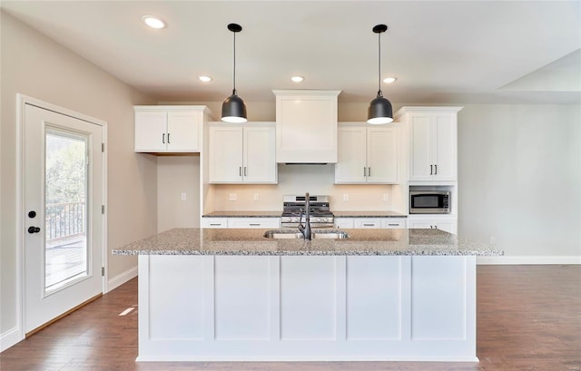 kitchen with a center island with sink, stone countertops, custom range hood, and appliances with stainless steel finishes