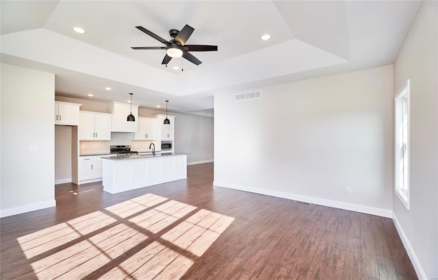 kitchen with a center island with sink, stainless steel range, decorative light fixtures, dark hardwood / wood-style flooring, and white cabinetry