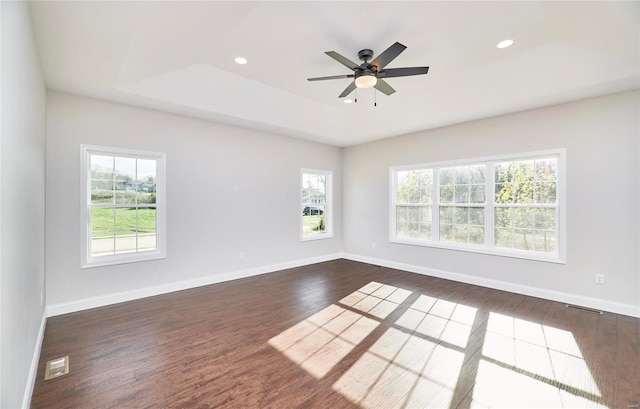 unfurnished room with ceiling fan, a raised ceiling, dark wood-type flooring, and a wealth of natural light