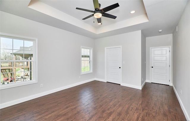 empty room with dark hardwood / wood-style flooring, a raised ceiling, and ceiling fan