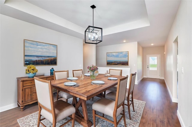 dining area with dark hardwood / wood-style floors, a raised ceiling, and an inviting chandelier