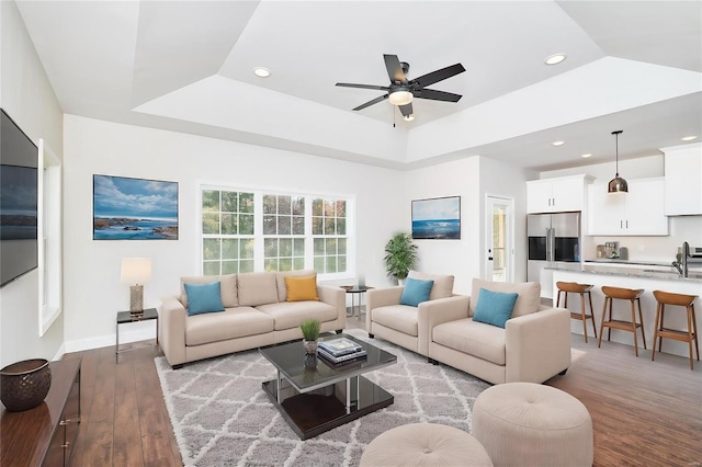 living room featuring ceiling fan, light wood-type flooring, sink, and a tray ceiling