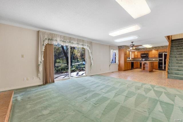 unfurnished living room featuring ceiling fan, light colored carpet, and ornamental molding