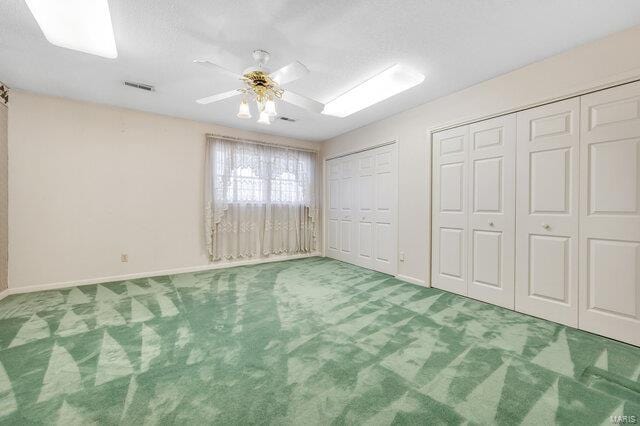 unfurnished bedroom with carpet, ceiling fan, and two closets