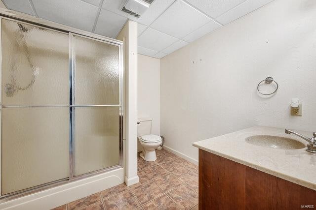 bathroom with a drop ceiling, tile patterned floors, toilet, a shower with door, and vanity