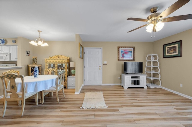 dining room with ceiling fan with notable chandelier and light hardwood / wood-style floors