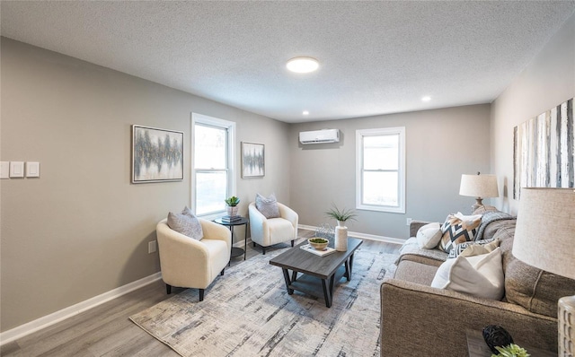 living room with a textured ceiling, a wall unit AC, and light hardwood / wood-style flooring