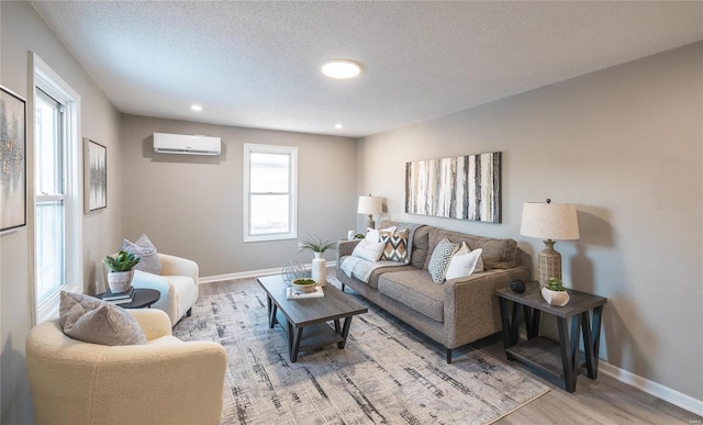 living area with a textured ceiling, a wall mounted AC, wood finished floors, and baseboards