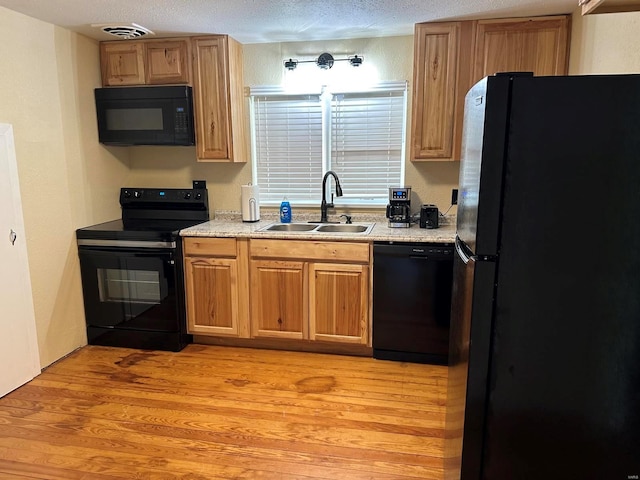 kitchen with black appliances, light wood-type flooring, sink, and a textured ceiling