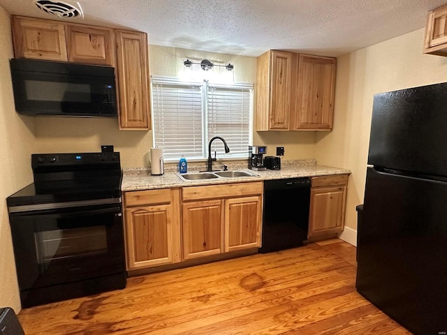 kitchen featuring black appliances, sink, light wood-type flooring, and a textured ceiling